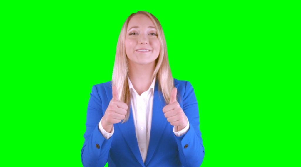 Young lady making the thumbs up gesture with a green screen behnd her.